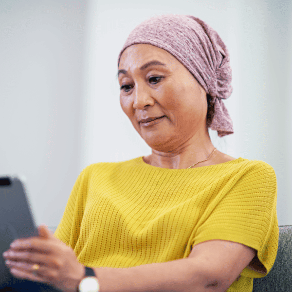 Asian woman with cancer with headwrap looking at a tablet with a Clario electronic clinical outcome assessment application open